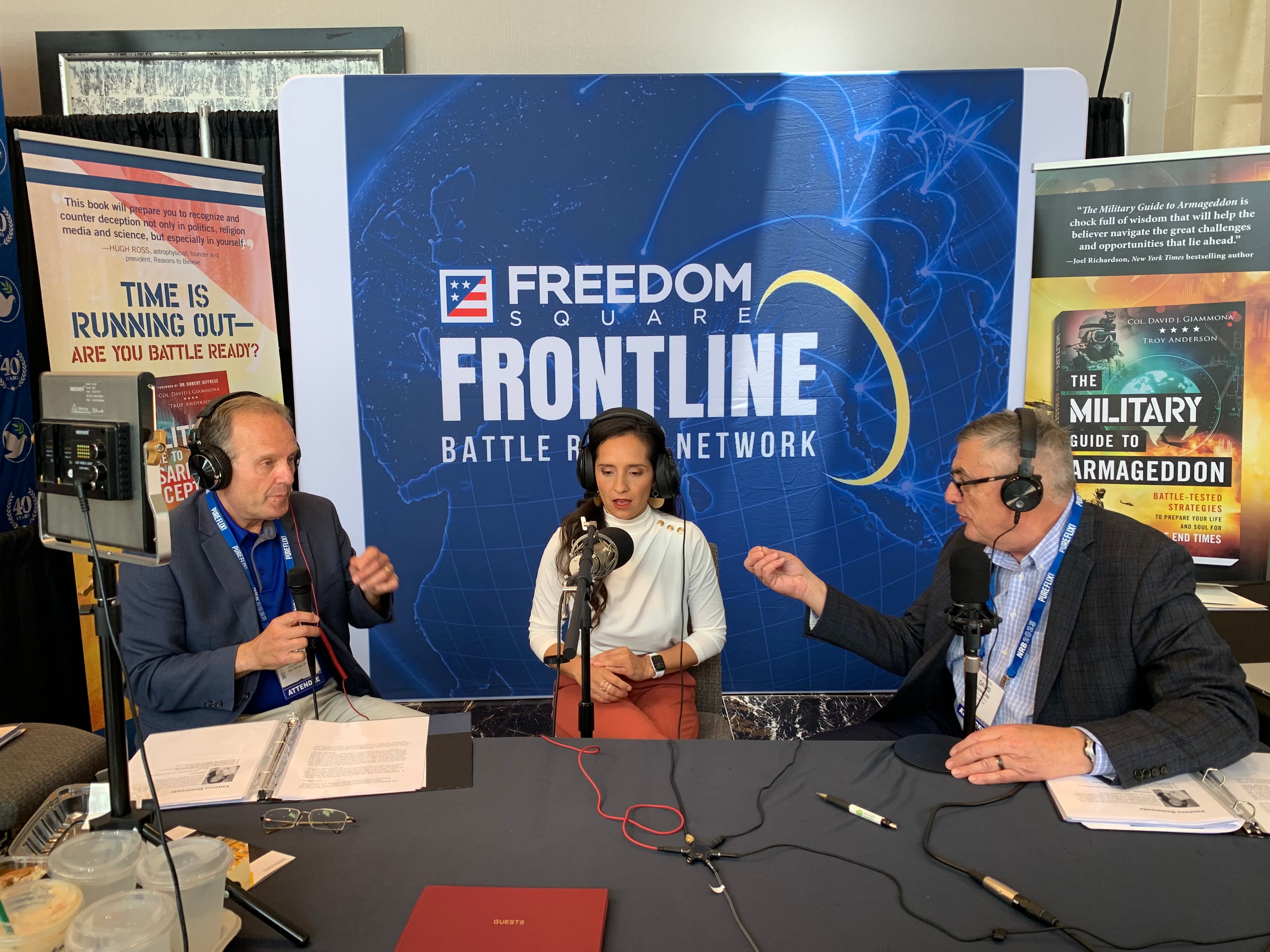 Three broadcasters wearing headsets speak into microphones at a Freedom Square Frontline media booth.