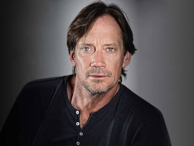 Headshot of a middle-aged man with blue eyes and brown hair wearing a dark shirt.