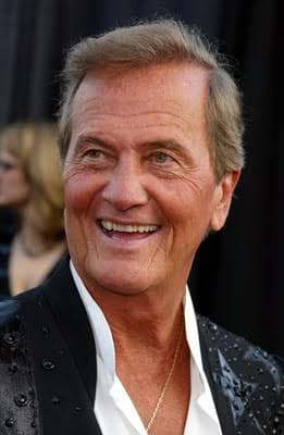 Smiling older man with light hair wearing a black studded jacket over a white collared shirt.