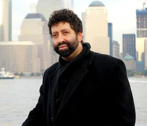 Bearded author Jonathan Cahn in a black coat with a city skyline in the background.