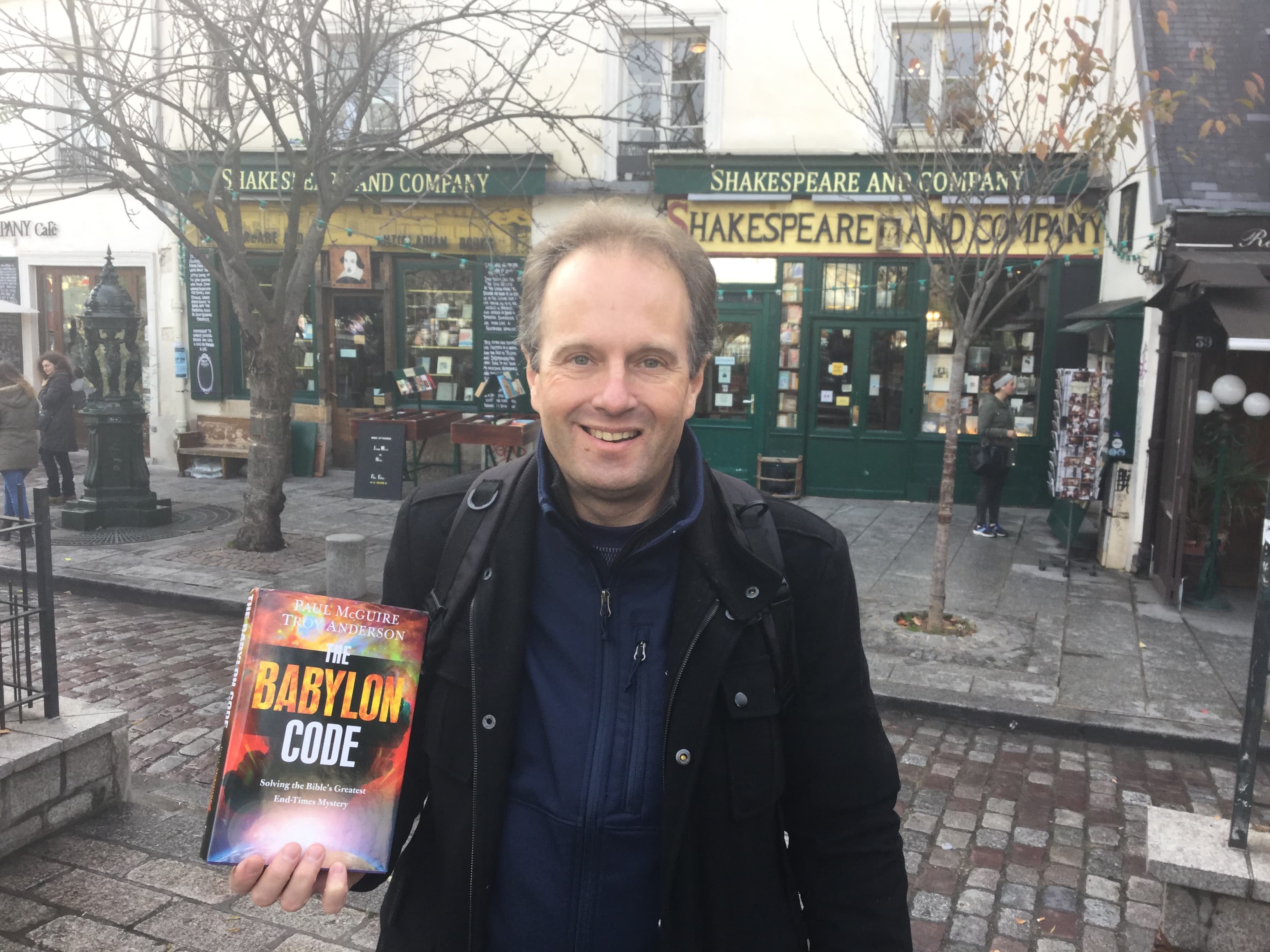 Smiling man holding The Babylon Code book in front of Shakespeare and Company bookstore.